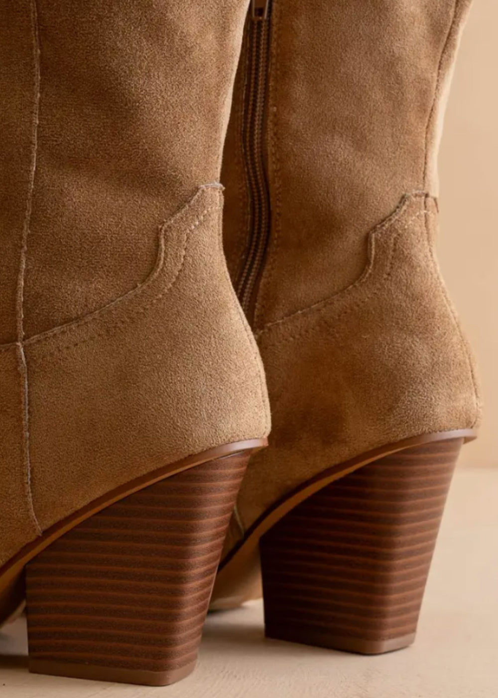 Close-up of brown suede boots with a beige background