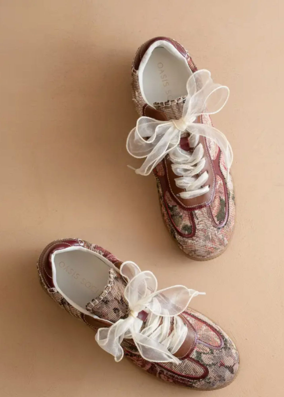 Pair of decorative shoes with white ribbons on a beige background