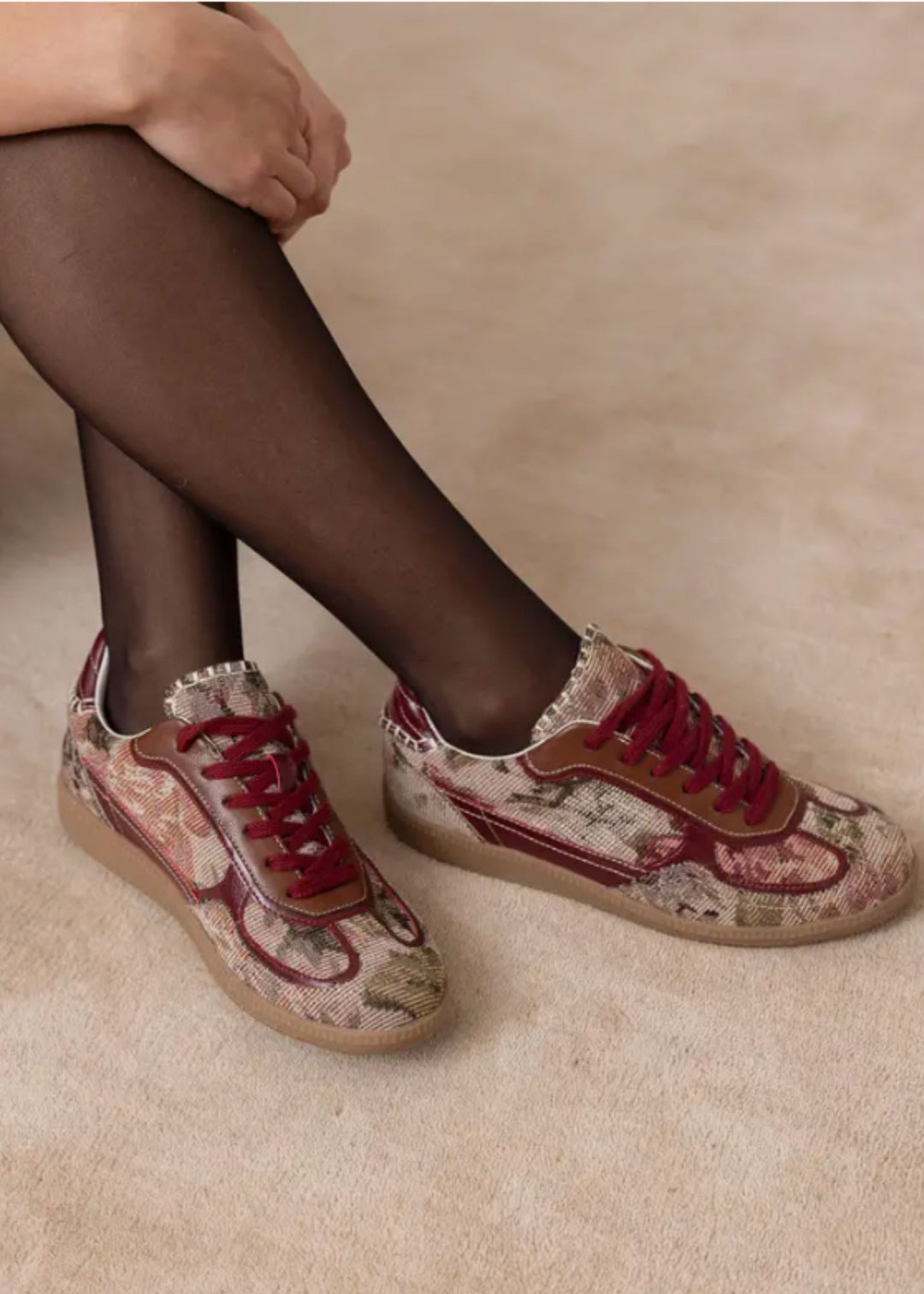 Floral sneakers worn with black tights on a beige background